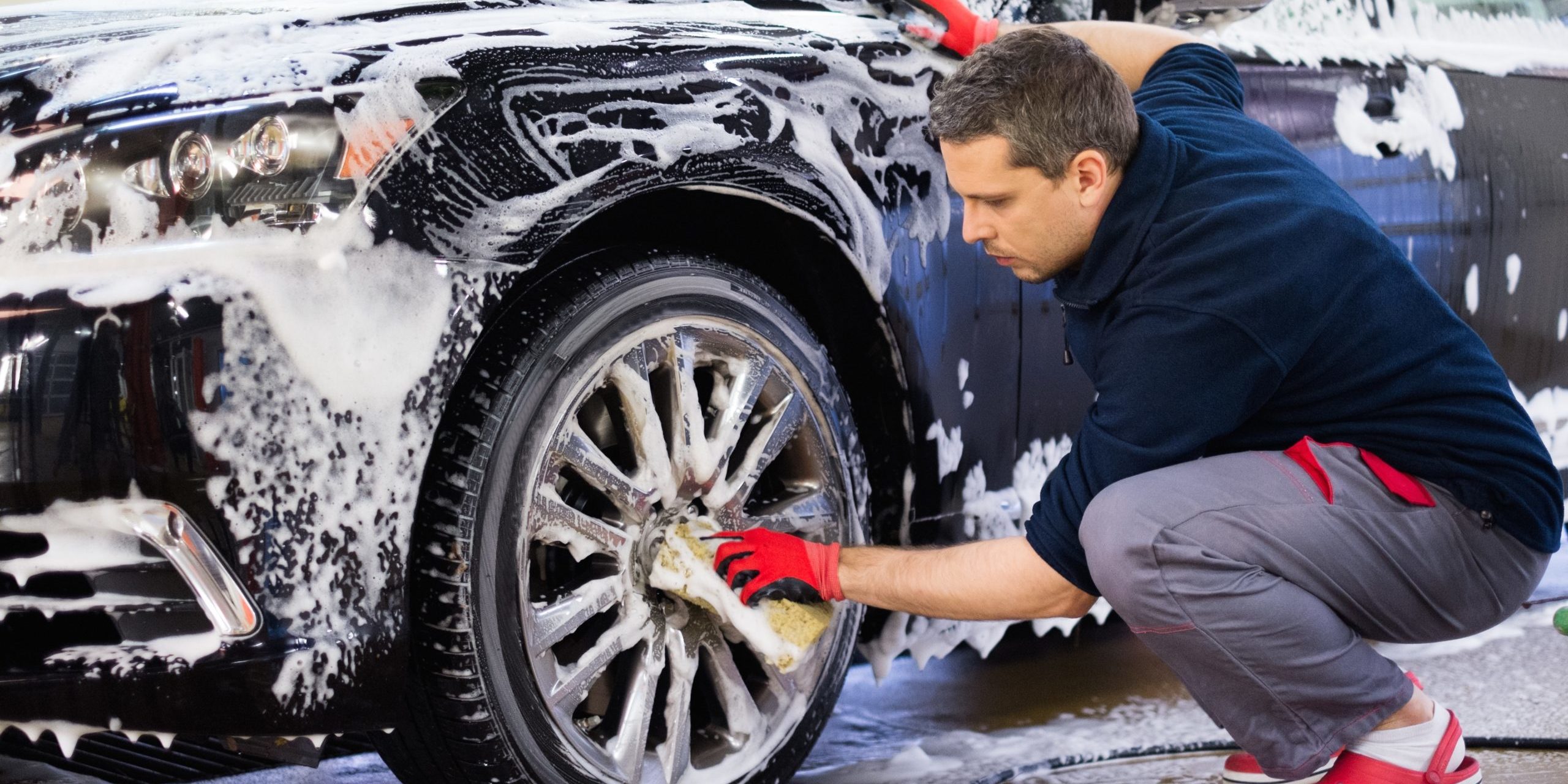 Man worker washing car's alloy wheels on a car wash